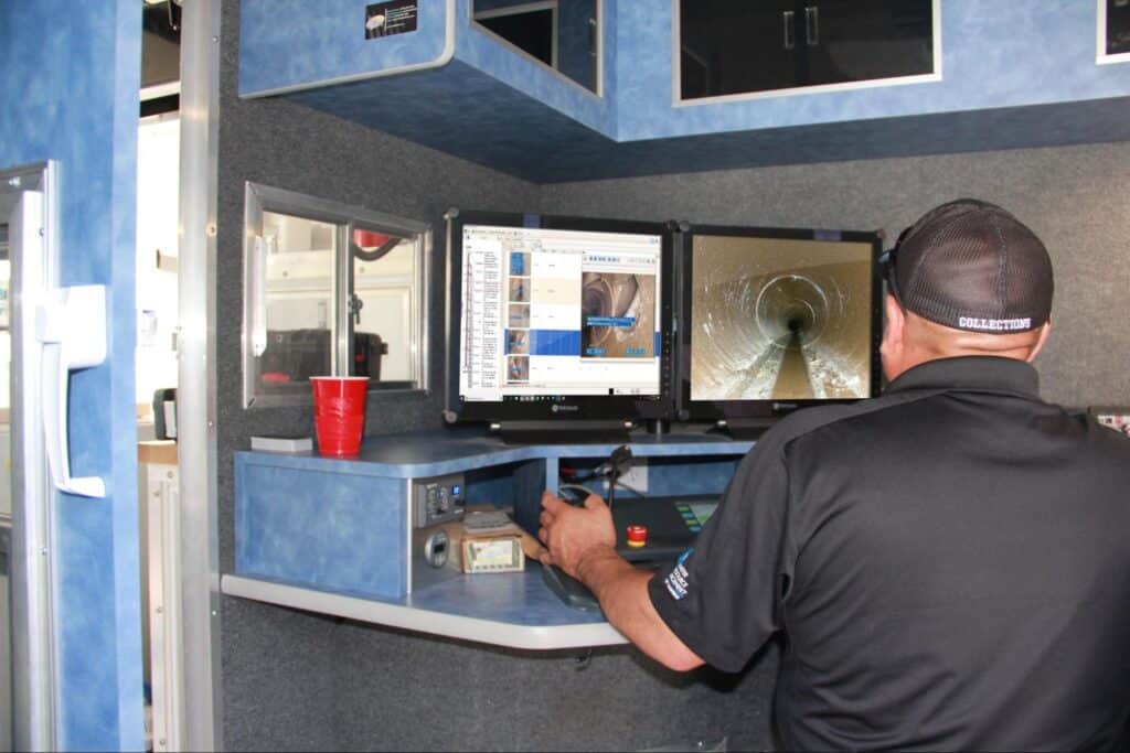 Technician using dual monitors for high-tech pipe inspection inside a service vehicle.