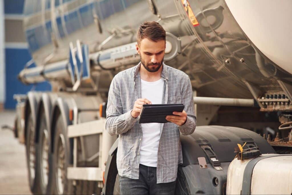 Man analyzing fuel efficiency data on a tablet next to a tanker truck.