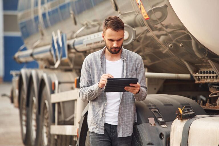 Man analyzing fuel efficiency data on a tablet next to a tanker truck.