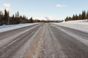 Snow-covered road winding through mountains under bright blue skies.