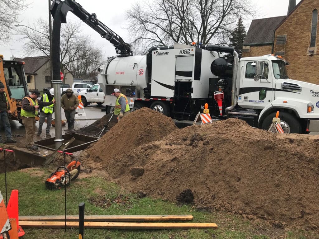 Sewer construction workers operating a vacuum truck at a digging site for drainage improvements.