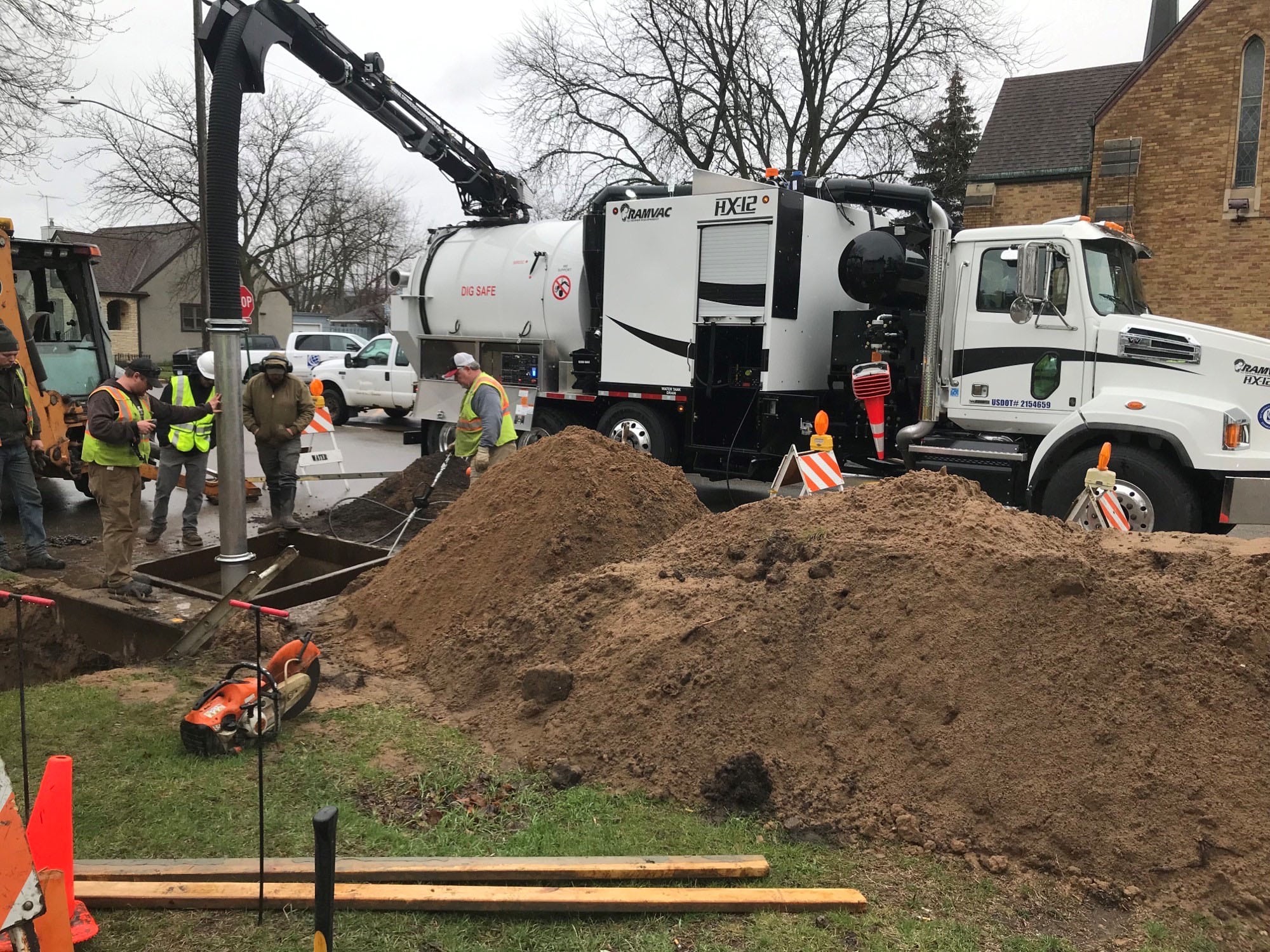 Sewer construction workers operating a vacuum truck at a digging site for drainage improvements.
