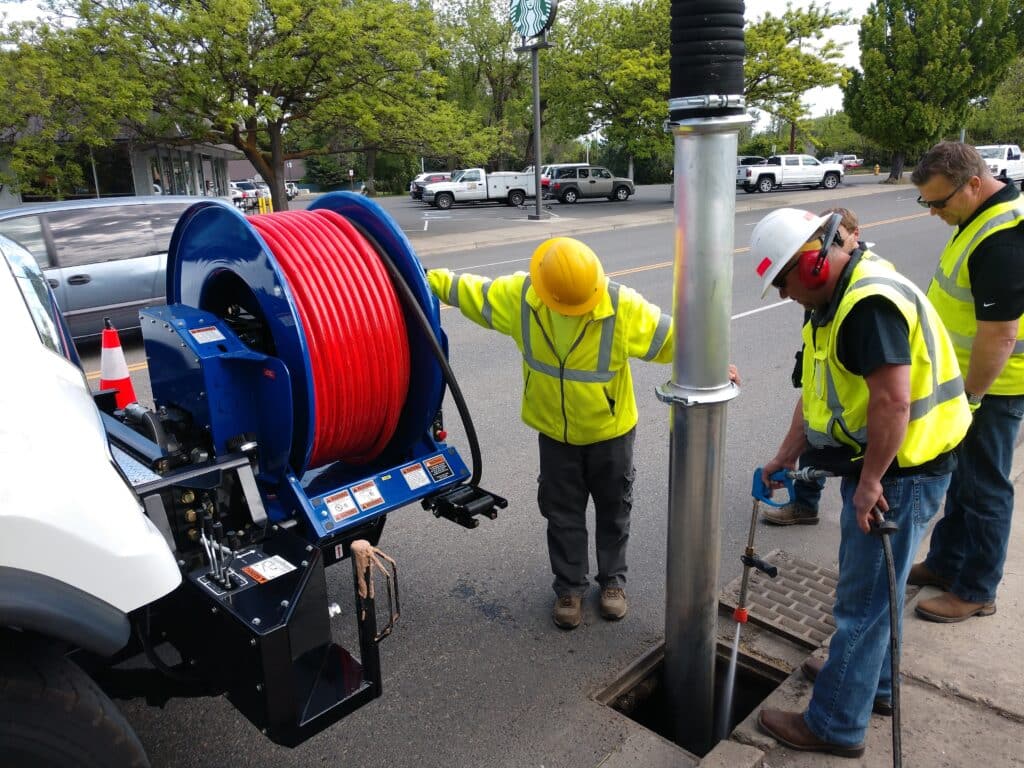 Combination sewer cleaning units used by professionals at a worksite, featuring a hose reel and crew.