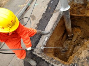 Worker using hydro-excavation to repair sewer lines at an urban construction site.