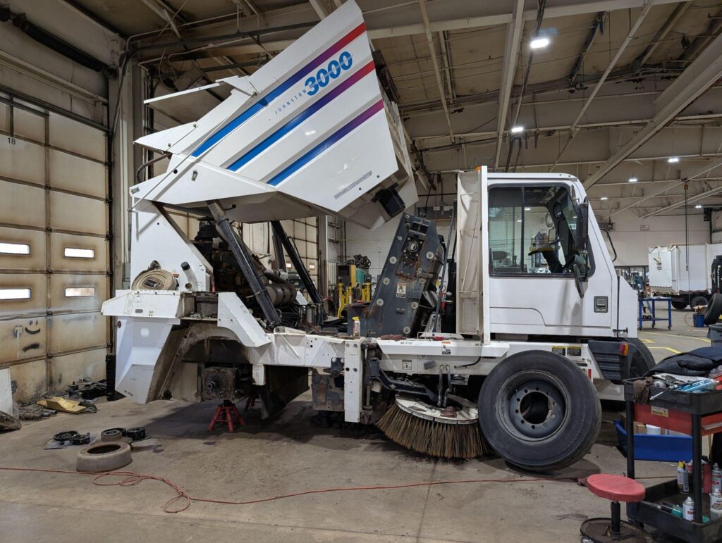 Street sweeper undergoing maintenance in a garage for essential repairs.