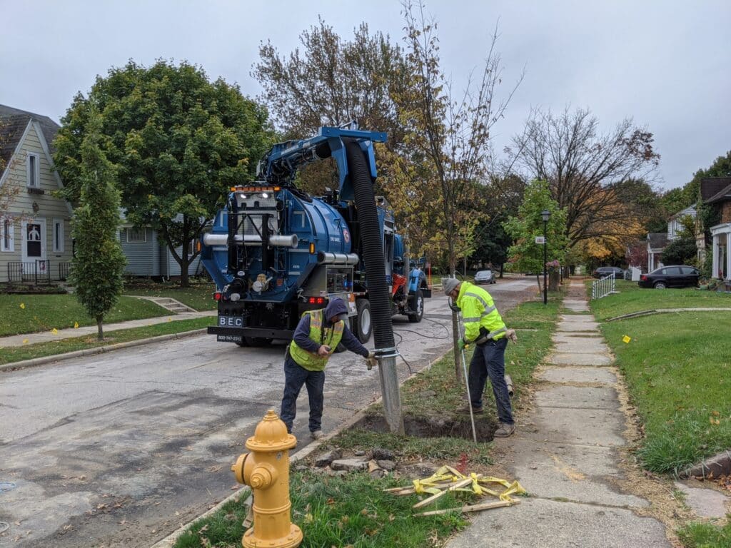 Sewer maintenance workers using specialized equipment near residential properties.