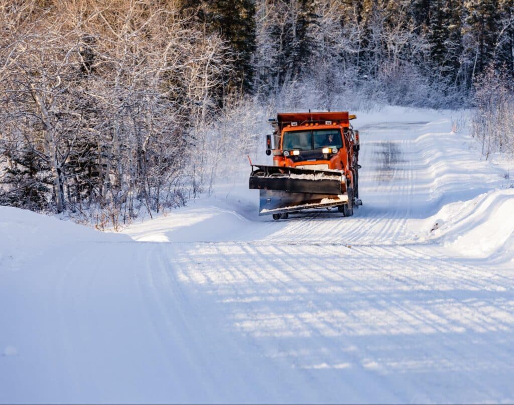 Snow plow clearing a snowy road through a winter landscape.