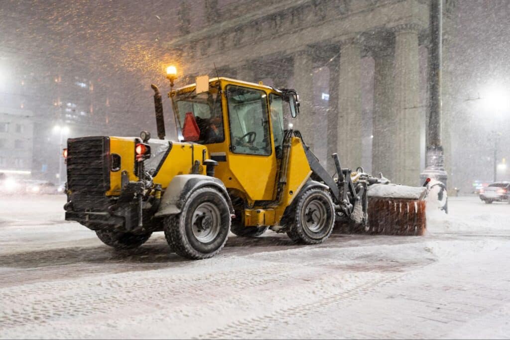 Snowplow clearing city streets during a heavy night snowstorm.