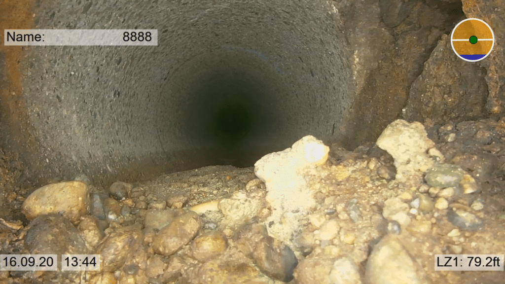 Close-up view of a smooth underground pipe with pebbles at the entrance.