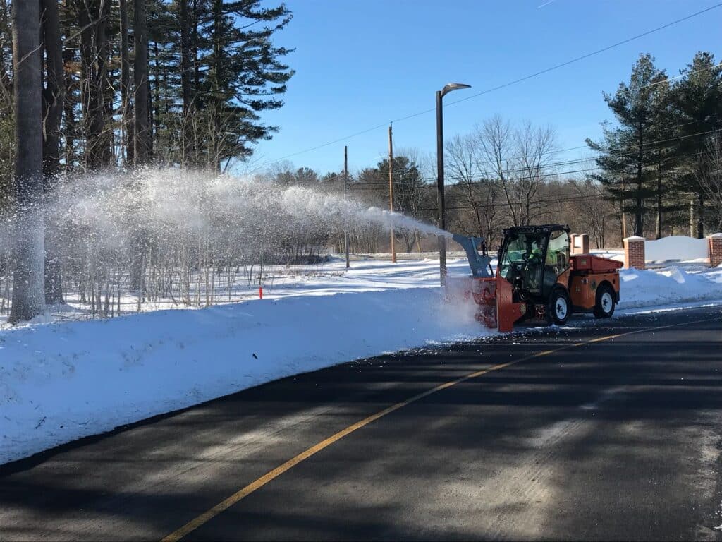 Multihog machine efficiently removing snow from a road in a wintery setting.