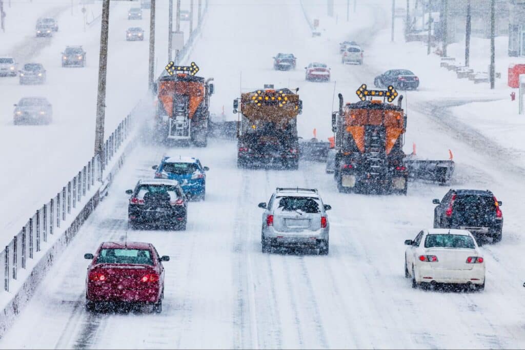 Snowplows clear highways as vehicles navigate through winter storm conditions.