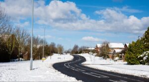 Snowy road in a tranquil neighborhood under a clear blue sky.