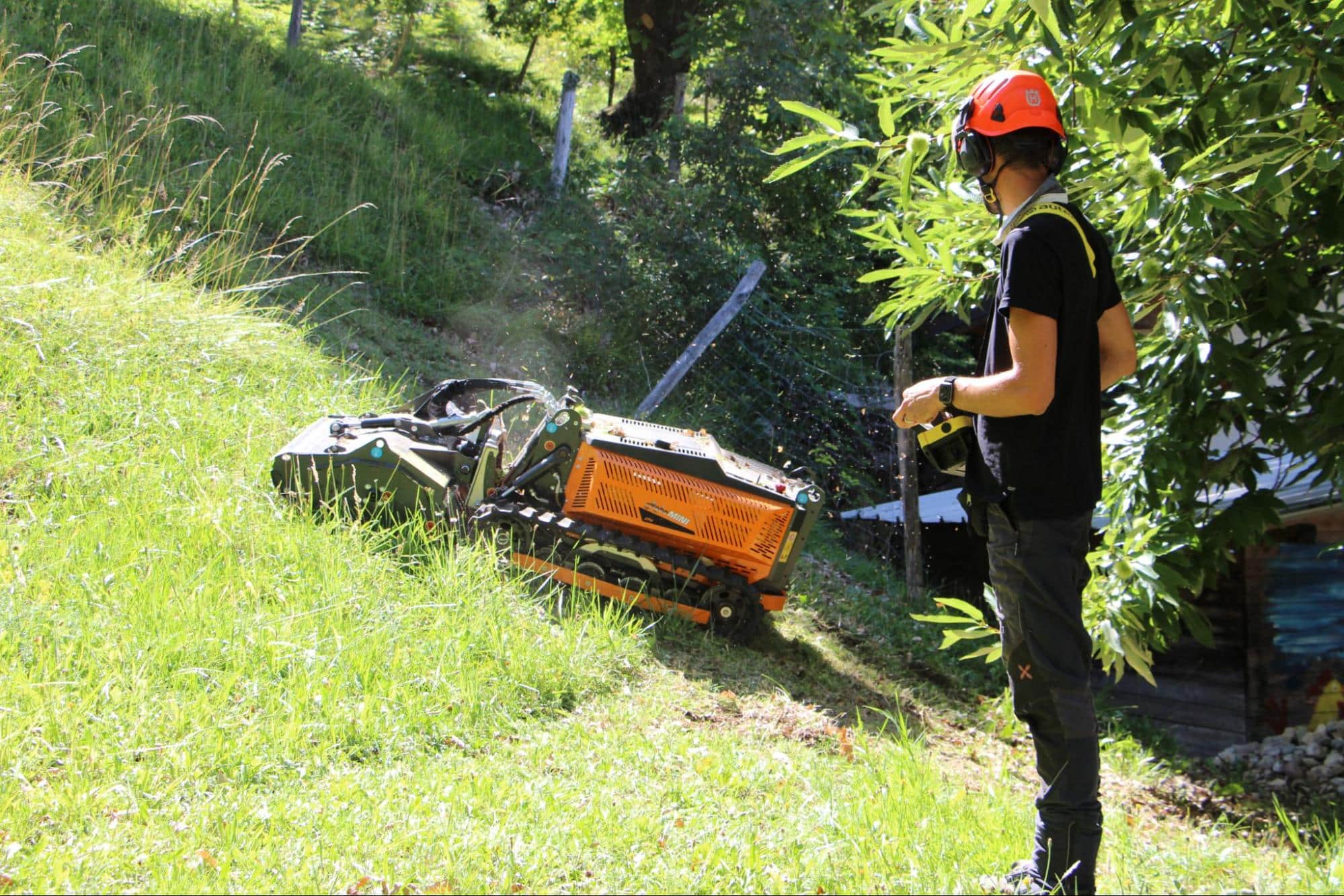 Operator using a hillside mower in a lush, steep landscape for safe lawn care.