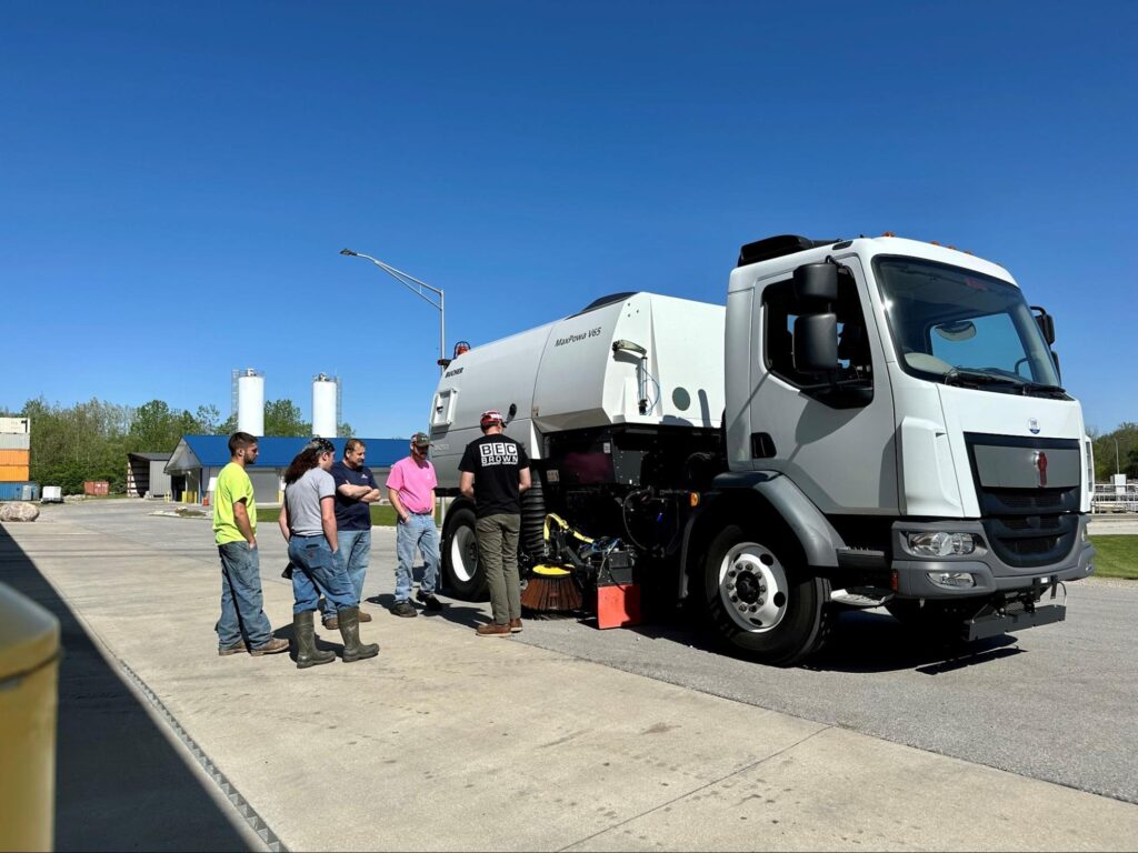 Workers examining a sanitation truck for maintenance on a sunny day.