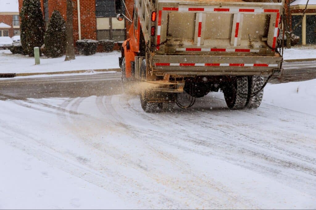 Snow plow spreading salt on icy roads during winter weather.
