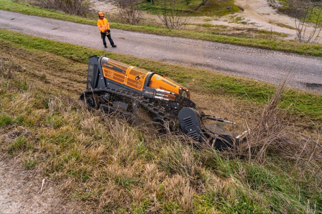 Energreen Robo machine efficiently clears grass and brush on hillside near gravel road.