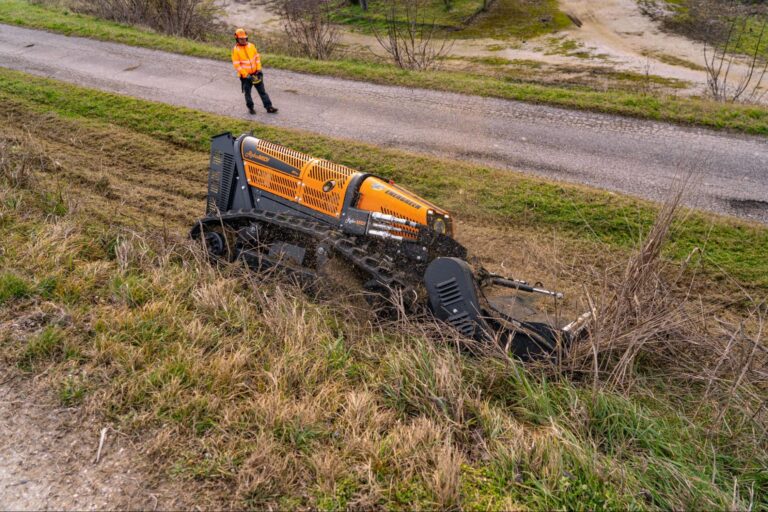 Energreen Robo machine efficiently clears grass and brush on hillside near gravel road.