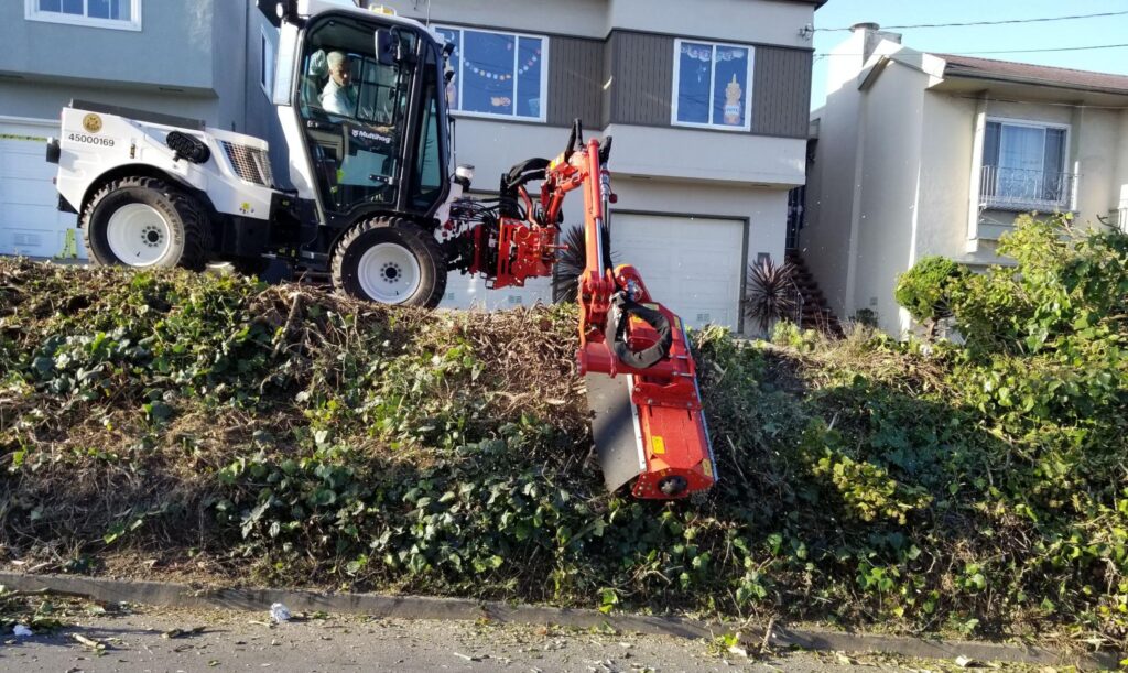 Heavy machinery clearing foliage for landscaping near residential homes.