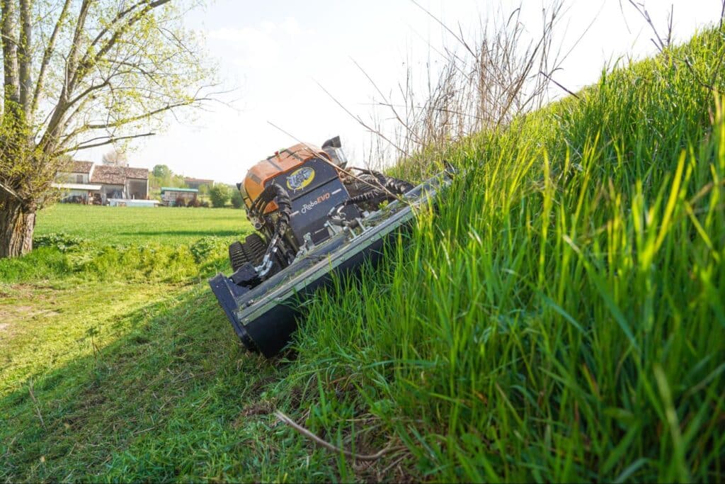 Remote-controlled mower efficiently navigating grassy slopes under clear skies.