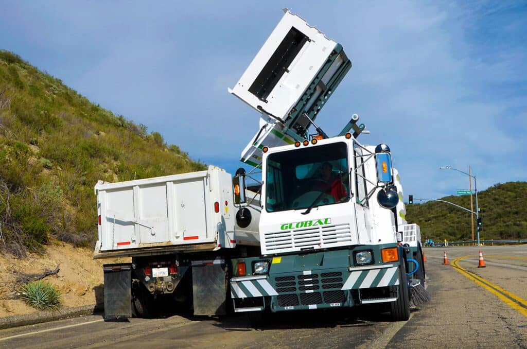 Street sweeper unloading collected debris on a rural road.